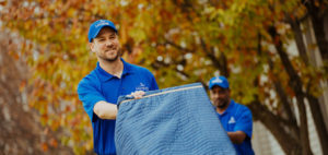 A mover pushing a dolly with pad wrapped furniture on it.