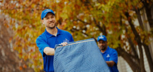 A mover pushing a dolly with pad wrapped furniture on it.