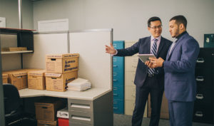 two men in suits in an office with Lawrence boxes stacked on the desk of the cubicle