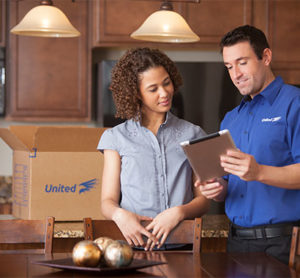 A man discusses with a woman in a kitchen while holding a tablet.