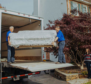 Two movers unloading a sofa out of a moving truck.