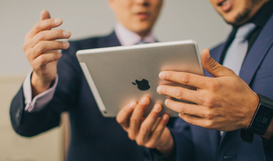 Two men in suits look at a tablet.