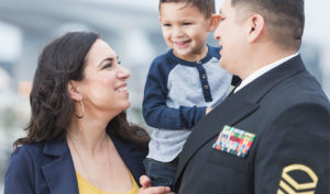 A soldier holds his kid while his wife smiles at him.