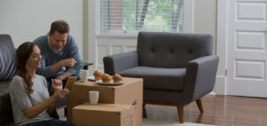 A couple sits in their living room and use boxes to sit their food on.