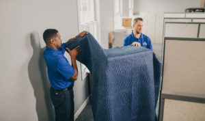 Two movers unwrapping a padded item.