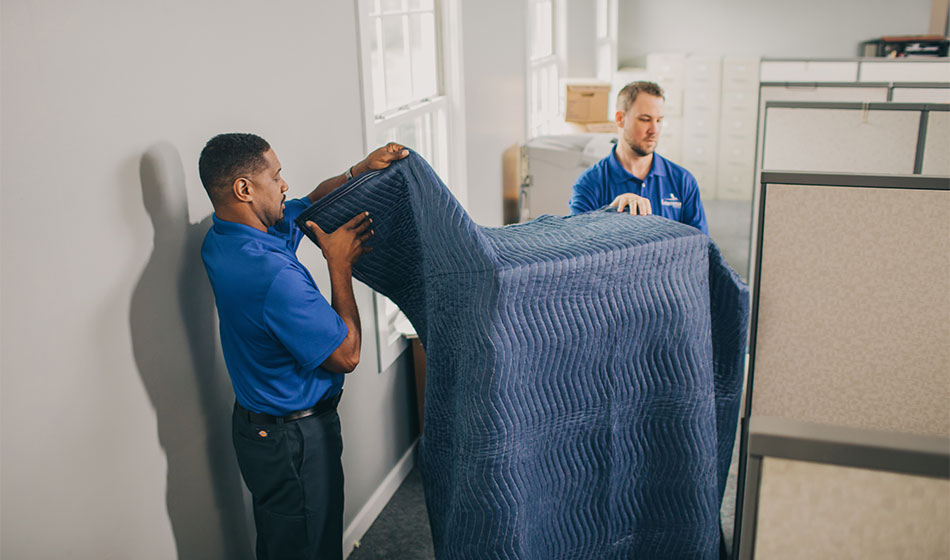 Two movers unwrapping a padded item.