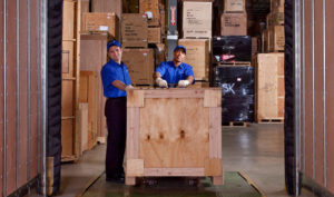 Two movers move a crate in a warehouse.
