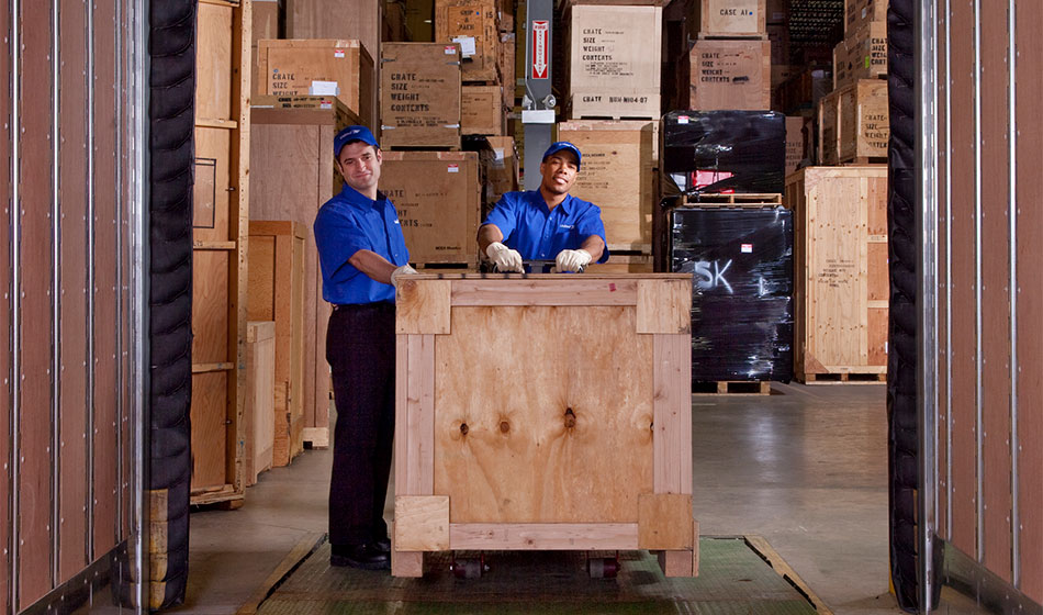 Two movers move a crate in a warehouse.