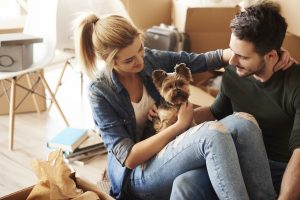 A Woman and man packing boxes taking a break to cuddle their dog