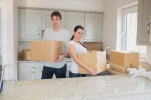 Man and woman holding moving boxes in a kitchen standing behind a kitchen counter.