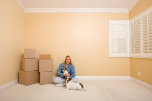 Woman and dogs sitting on the floor with moving boxes in empty room.