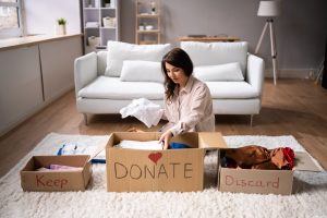 Woman sitting on the floor sorting items into boxes for donating, keeping, and discarding.
