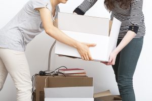 One person stretching out arms handing a moving box to another person while packing for a move.