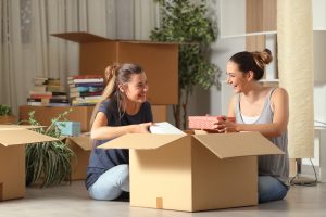 two female roommates sitting on the floor packing ups a moving box.
