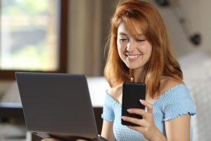 Smiling woman working in a hotel room using her laptop and mobile phone.