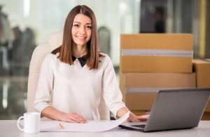 Woman in office with moving boxes in the background and a laptop in the foreground.