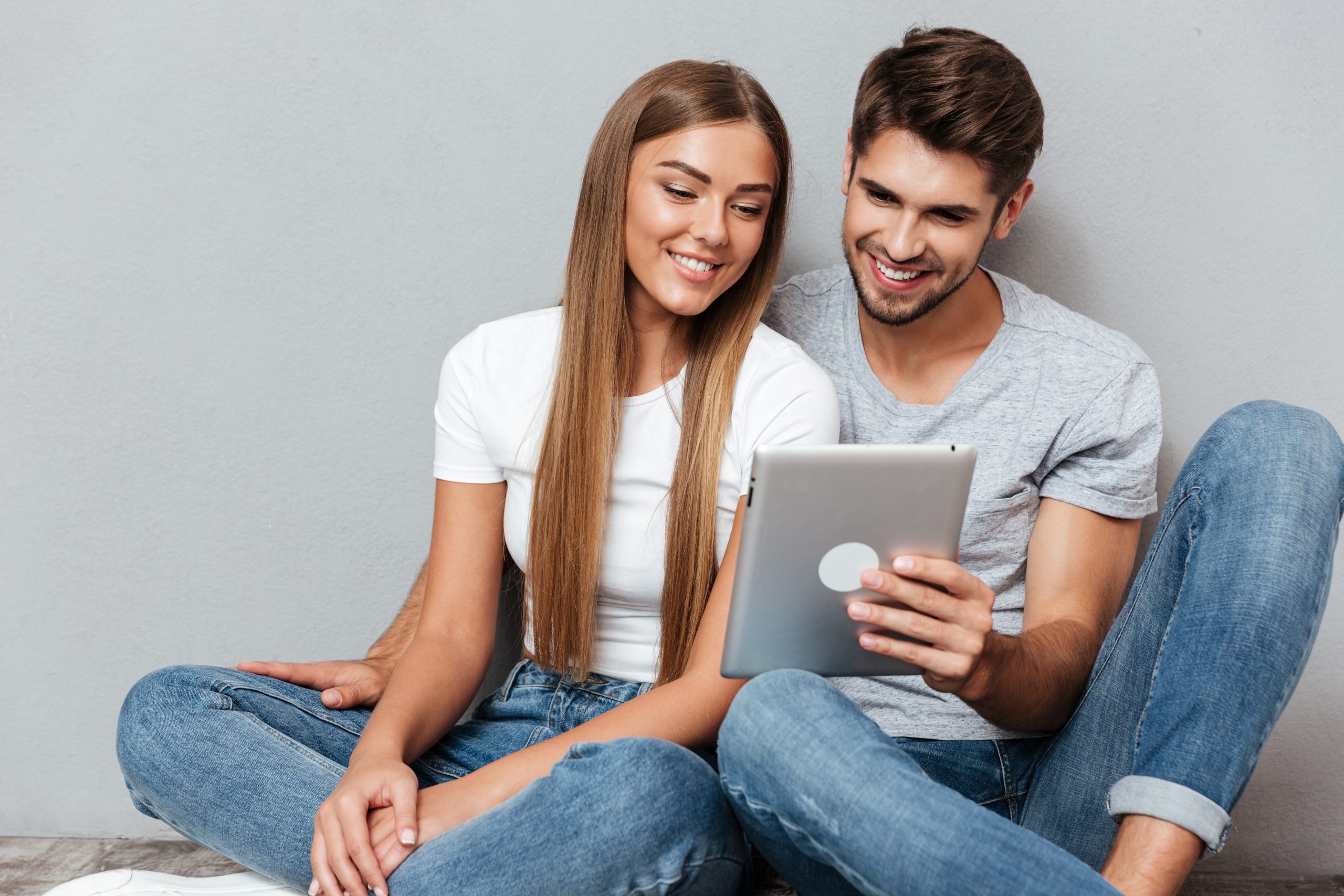 Woman and Man in jeans sitting on floor reviewing something on a tablet