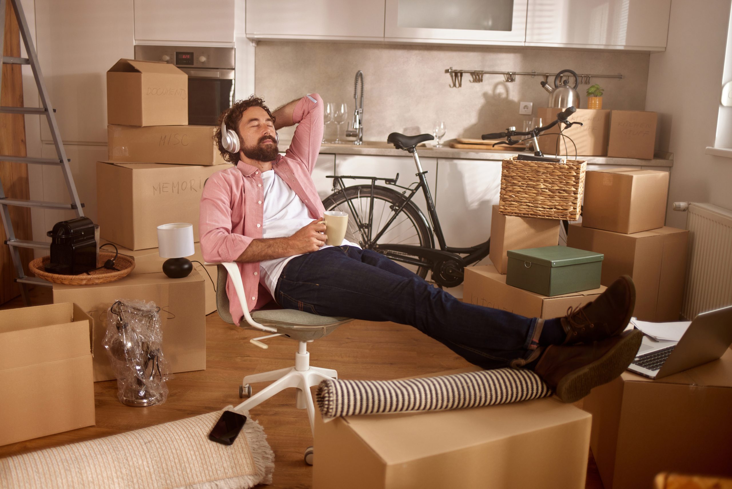 Moving day at the new home with a man relaxing among boxes and unpacked items as he listens to music